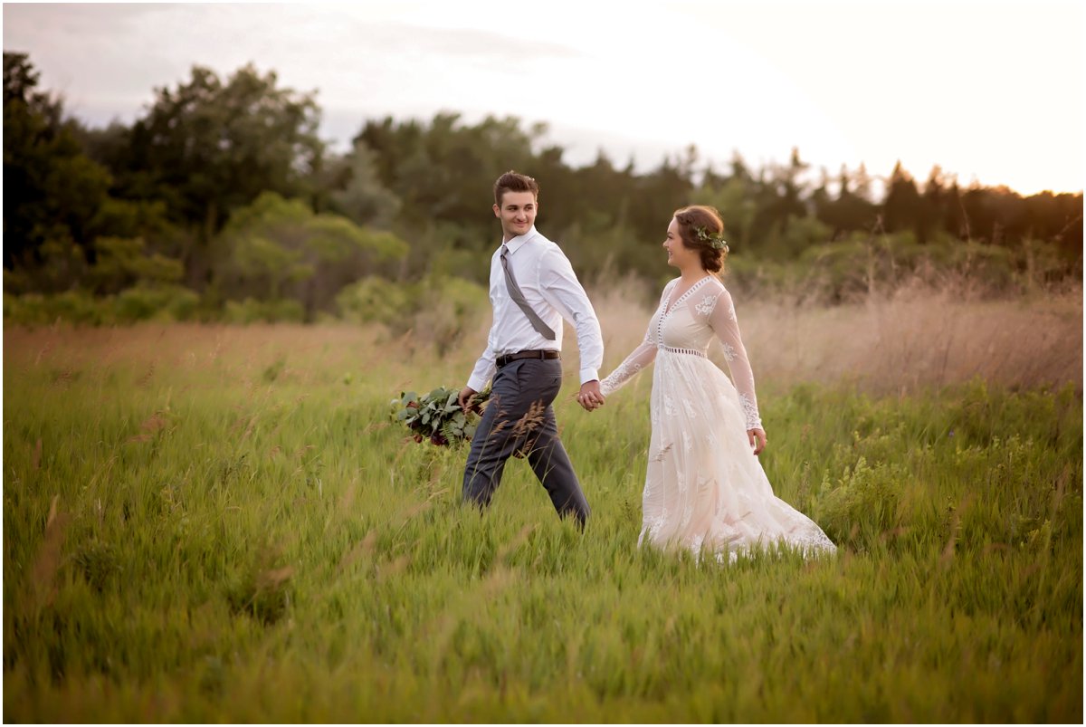 boho groom holds brides bouquet and walks