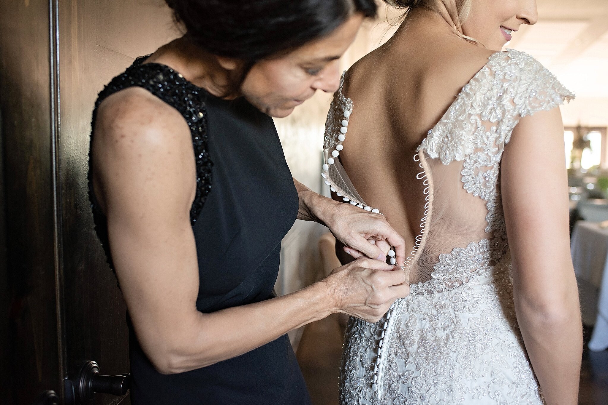mother of the bride wears long black sleeveless formal gown to help bride get ready